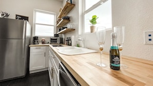 A modern kitchen with stainless steel appliances, wooden countertops, and a window with a plant.