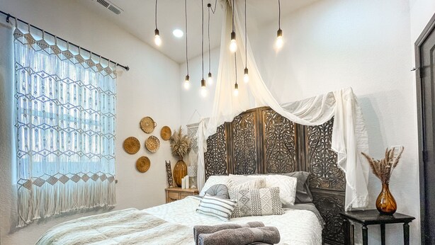 A bedroom with a large bed, a bedside table, a decorative headboard, and a window with curtains.