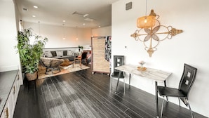 A modern living room with dark wooden flooring, a sofa set, a dining table with chairs, and a decorative wall piece.