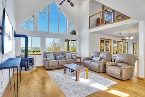Un salón amplio con techos altos, ventanas grandes, chimenea y sofás de cuero.