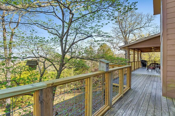 A wooden deck with a railing, overlooking a forested area with trees and a clear sky.