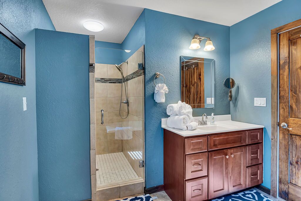 Un baño con ducha de vidrio, tocador de madera con espejo y pared azul.