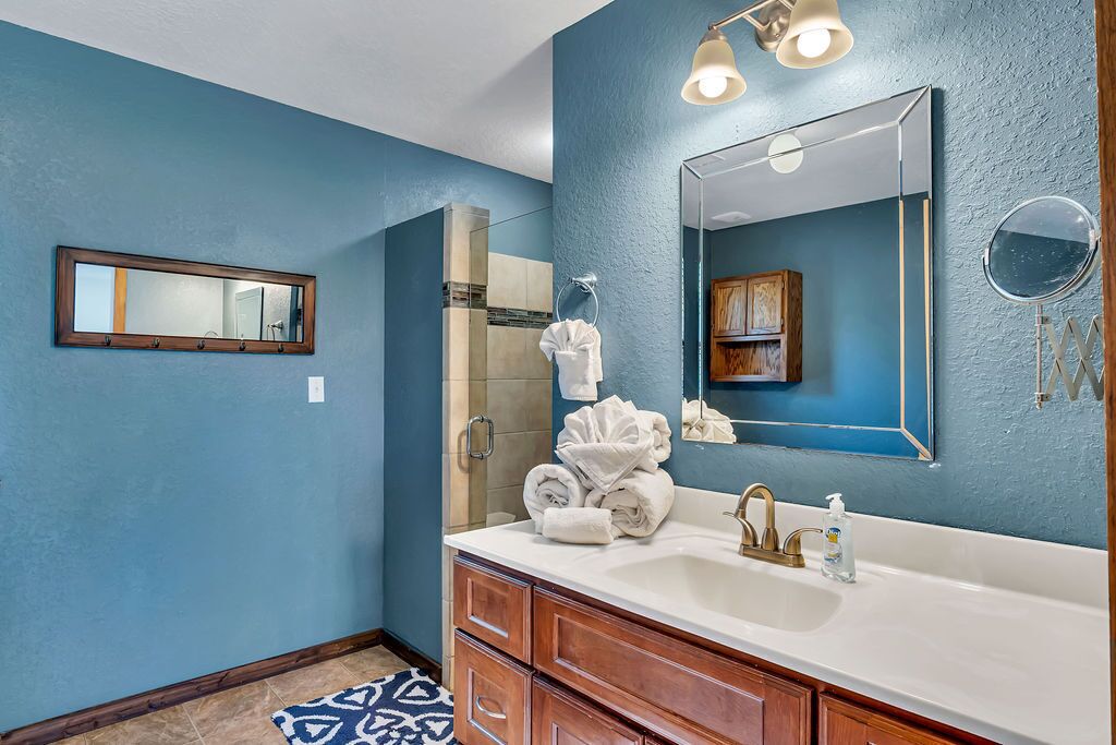 A bathroom with a blue wall, a large mirror, a white sink, and wooden cabinets.