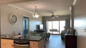 A modern kitchen with a dishwasher, a clock, and a dining area with a sofa and a TV. - Top-Floor Condo - On the Beach - Gulf Views - Walk the Boardwalk (Biloxi)