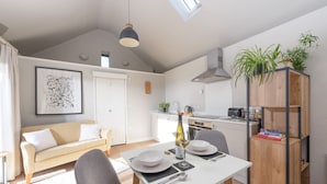 Une cuisine moderne avec un coin repas, une chambre à coucher aménagée en mezzanine et un salon doté d’un canapé et d’un tableau.