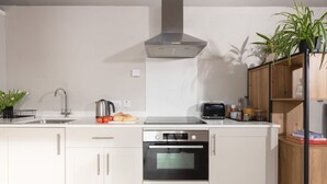 Une cuisine moderne équipée d’un four encastré, d’une hotte en acier inoxydable, d’un évier et d’un plan de travail sur lequel se trouvent une bouilloire, des tomates et du pain.