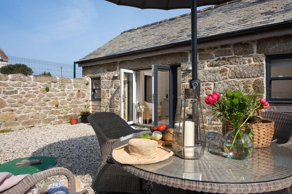 A stone building with a glass door, wicker furniture, and a table with a vase of flowers.