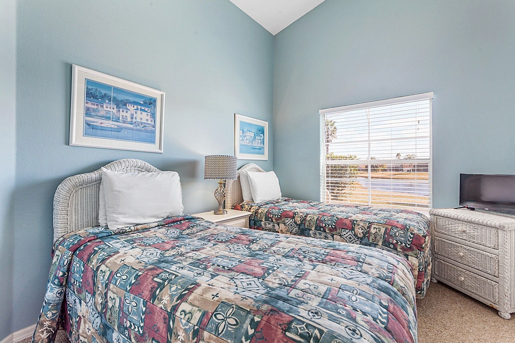 A bedroom with two beds, a nightstand, a lamp, a dresser, and a television.