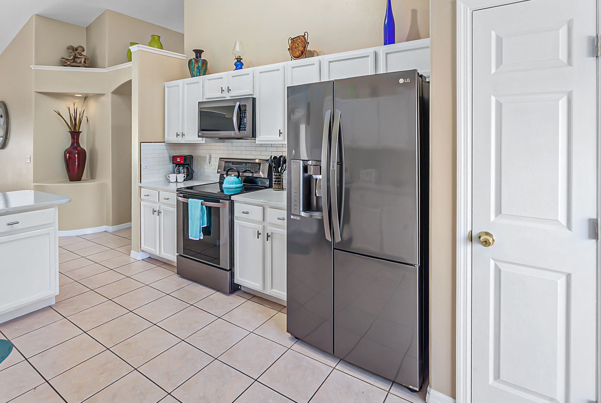 A modern kitchen with white cabinetry, a stainless steel refrigerator, an oven, and a microwave.