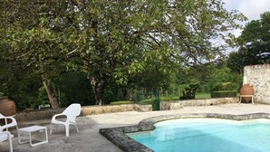 A swimming pool with a stone border, surrounded by a paved patio with white plastic chairs and a table. - charming apartment in a 16th century mansion (Allemans)