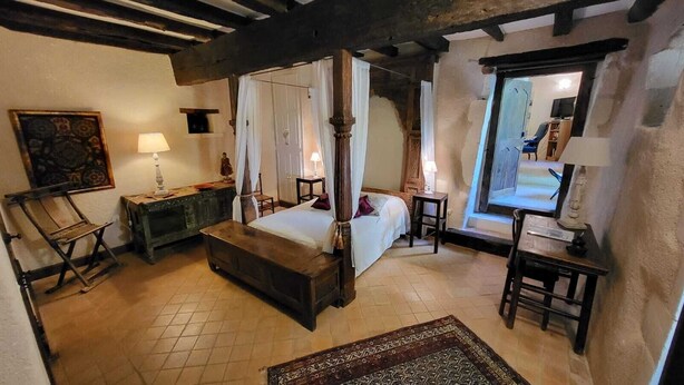A traditional four-poster bed with a canopy, a wooden bench, a small table, and a chair in a rustic room with exposed beams and a tiled floor. - charming apartment in a 16th century mansion (Allemans)
