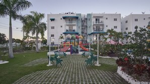 A playground with slides and benches, surrounded by a paved area and palm trees. - Tropical getaway (Santiago De Los Caballeros)