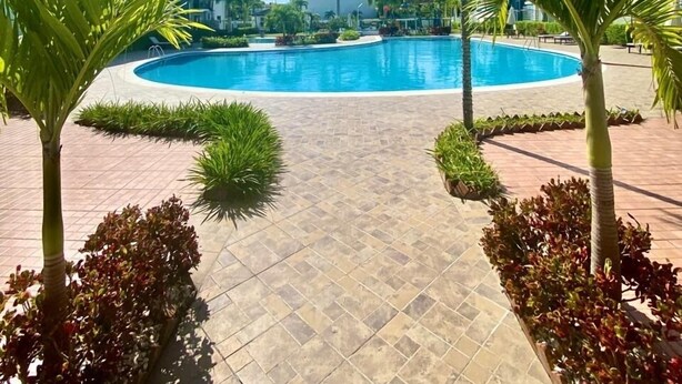 A swimming pool surrounded by palm trees and a tiled walkway. - Tropical getaway (Santiago De Los Caballeros)