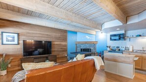 A modern living room with a large TV, a fireplace, and a kitchen area with a bar.