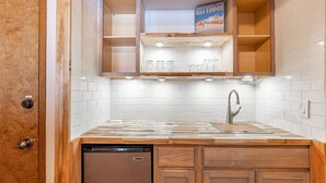 A compact kitchen with a built-in dishwasher, wooden cabinets, and a shelf with glassware.
