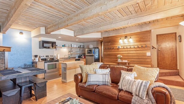 A modern kitchen with a central island, a brown leather sofa, and a wooden wall with built-in lighting.