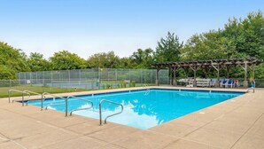 Una piscina rectangular con barandillas metálicas, rodeada por una cerca y árboles.