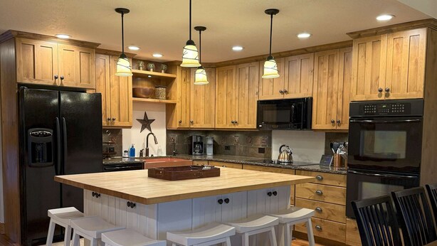 Una cocina moderna con armarios de madera, un refrigerador negro, horno empotrado y una isla central con taburetes de bar.