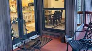 Un espacio exterior techado con sillas de metal y una mesa, una terraza de madera y vistas hacia una cocina con armarios de madera y una araña.