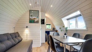 Un interior acogedor y moderno con techo de madera, un comedor con mesa y sillas, un sofá y una pequeña cocina.