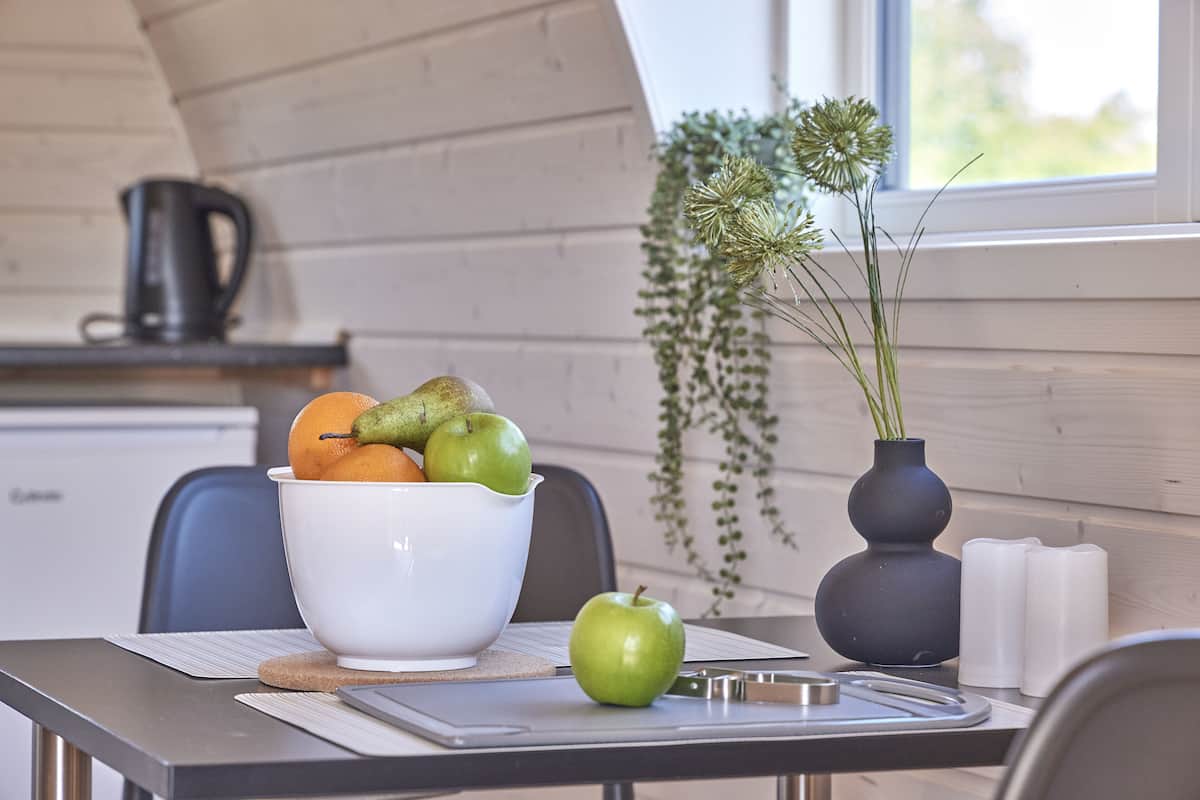 A kitchen with a white bowl containing fruits, a green apple, and a black kettle on the counter.