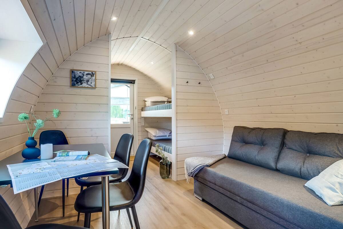 A cozy cabin interior with a dining table, chairs, a sofa, and a bunk bed.