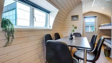 Een gezellige kamer met een houten inrichting, een eettafel met stoelen, een stapelbed en een raam met uitzicht op een gebouw.
