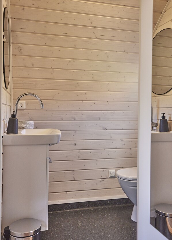 A bathroom with a wooden wall, a sink, a toilet, and a trash can.