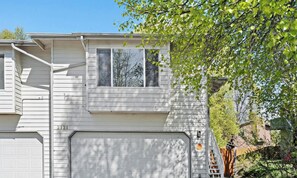 Une maison à deux étages avec un garage, un numéro de maison bien visible et un arbre au premier plan.