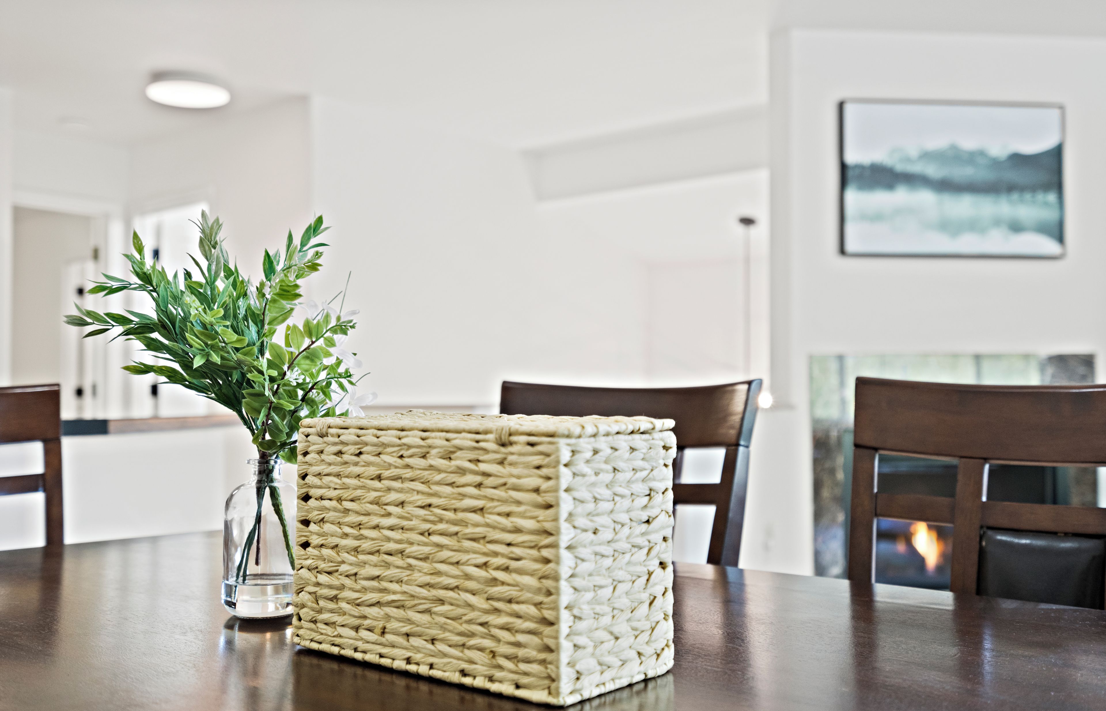 A dining table with a woven basket and a vase of greenery.
