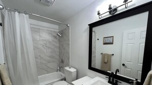 Un baño moderno con bañera, inodoro, lavabo y un espejo grande.
