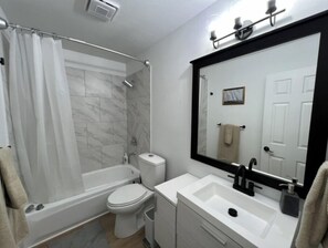 Ein modernes Badezimmer mit Badewanne, Toilette, Waschbecken und einem großen Spiegel.