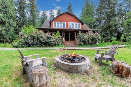 A house with a fire pit in the front yard, surrounded by wooden chairs and a log.. Large Lodge Near Nisqually Entrance, Sleeps 18