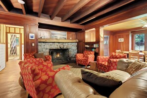 A cozy cabin interior with a stone fireplace, leather sofas, and a wooden ceiling.