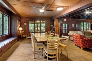 A spacious room with a large wooden dining table, multiple chairs, a ceiling fan, and a sofa.