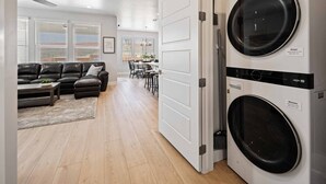Ein moderner Waschraum mit einer Frontlader-Waschmaschine und einem Trockner, ein Essbereich mit Tisch und Stühlen sowie ein Wohnzimmer mit einer Ledersofa und einem Couchtisch.