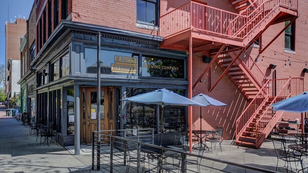 A brick building with a sign for 'Natty's Brewing Company' and outdoor seating with umbrellas.