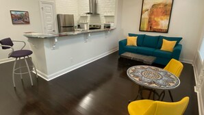 A modern kitchen with white brick backsplash, stainless steel appliances, and a dining area with a round table and yellow chairs.
