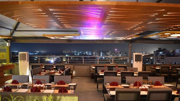 A rooftop restaurant with tables set for dining, a city view, and a modern ceiling design.