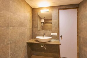 A bathroom with a white sink, a mirror, and a shower stall. - 7Wonders Hotel (Gandhinagar)
