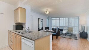 A modern kitchen with granite countertops, a dishwasher, and wooden cabinets. There is a dining area with a sofa and a coffee table. The room has large windows with blinds. - 2 Bedroom/2 Bathroom Suite (Scarborough)