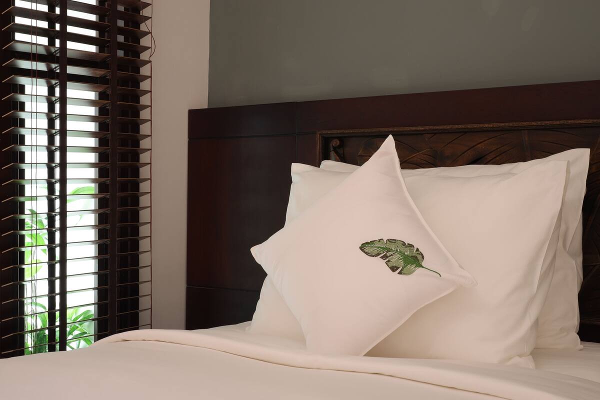 A neatly made bed with white bedding and a single decorative pillow featuring a leaf design.