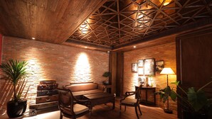 A cozy room with a wooden ceiling, brick walls, a sofa, chairs, a table, and potted plants. - Cochin Sang Hotel (Ho Chi Minh City)