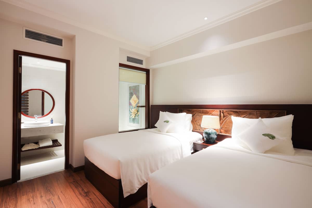 A hotel room with two beds, a bathroom with a mirror, and a window with a view.
