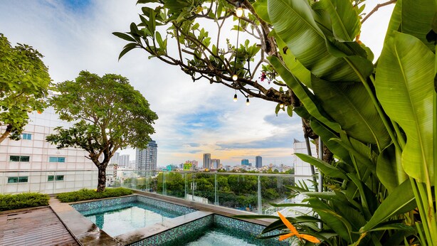 A rooftop pool with a city skyline view, surrounded by lush greenery and a wooden deck. - Cochin Sang Hotel (Ho Chi Minh City)
