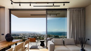 Un salon moderne avec un canapé, une table à manger et des chaises. De grandes fenêtres offrent une vue sur le paysage urbain.