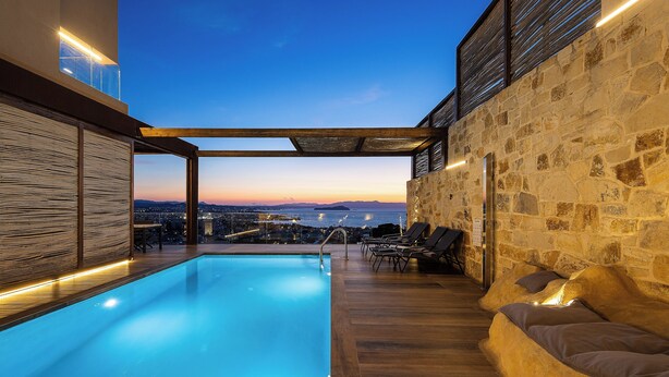 Une piscine sur le toit offrant une vue sur la ville au crépuscule, une terrasse en bois et un mur en pierre.