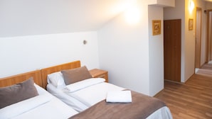 A hotel room with two beds, wooden headboards, white bedding, a wooden floor, and a hallway with wooden doors. - Romantic attic 1/3 room  (Izola)