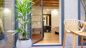 A modern interior with a potted plant, a wicker chair, and a glass door leading to a room with a wooden floor.