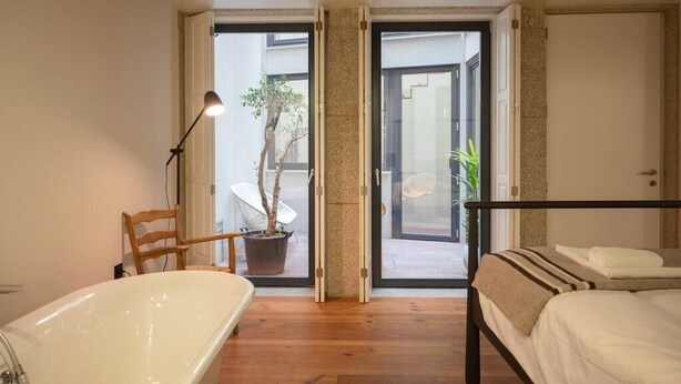 A modern bedroom with a large bathtub, a bed, and a chair.